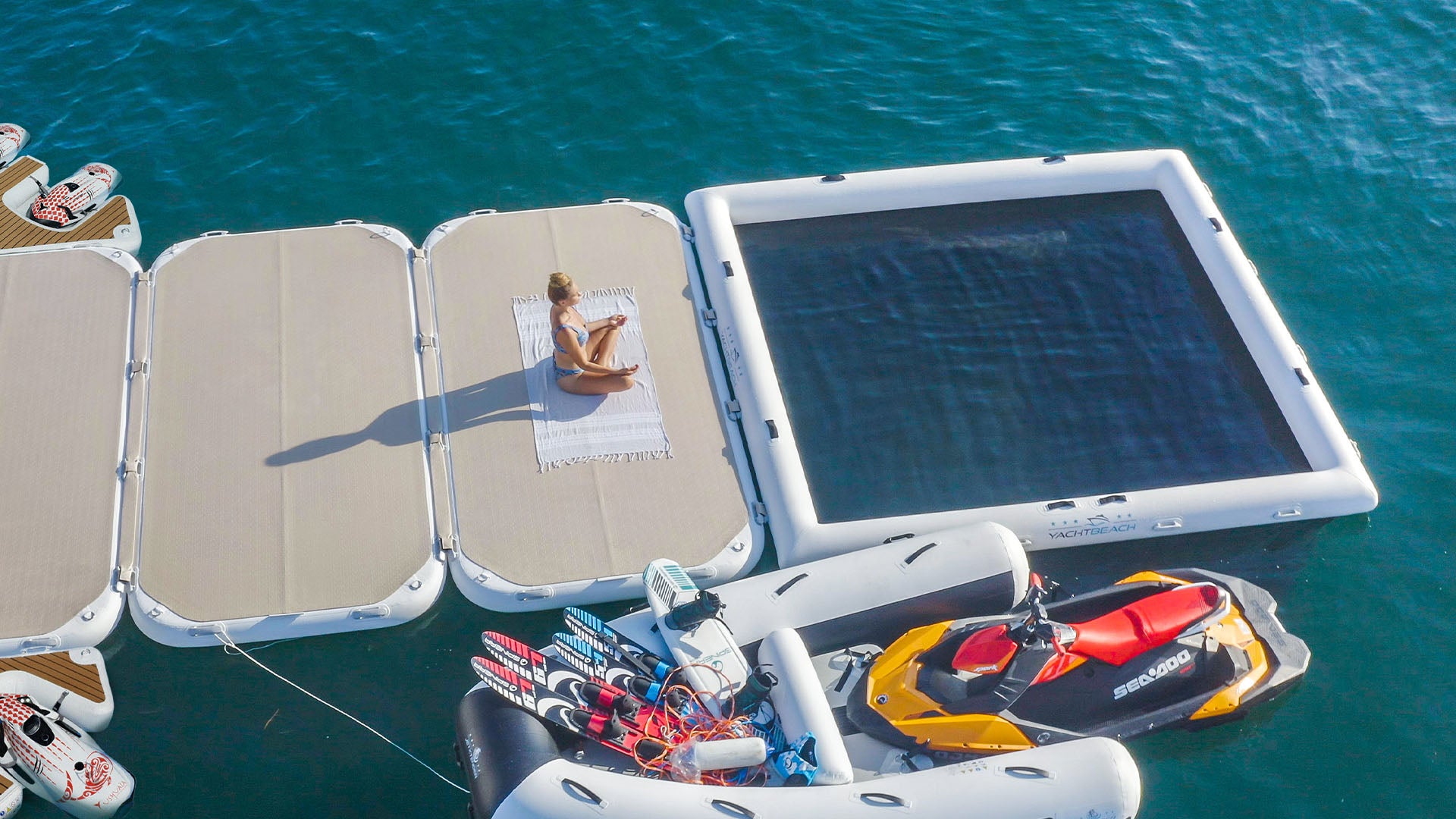 Three yacht beach platforms and a pool frame are attached to a boat on the water, on which a woman is sunbathing.