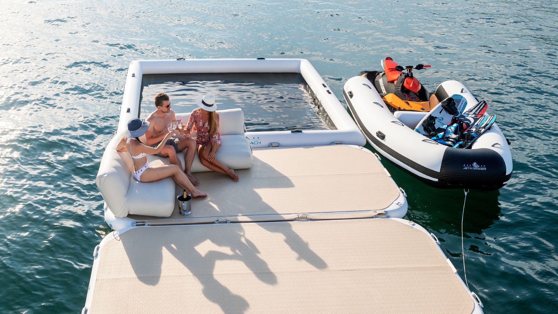 The picture shows a pool frame and two yacht beach platforms on which three people have made themselves comfortable on an inflatable couch. There is also a jet ski on the water.