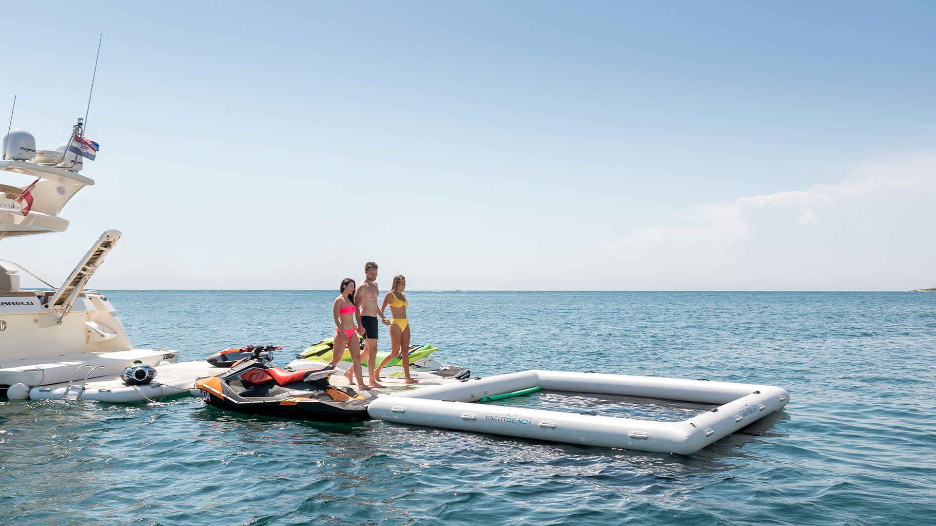 The picture shows a boat on the water with two yacht beach platforms and a pool frame attached to it. Three people are walking hand in hand on the platform.