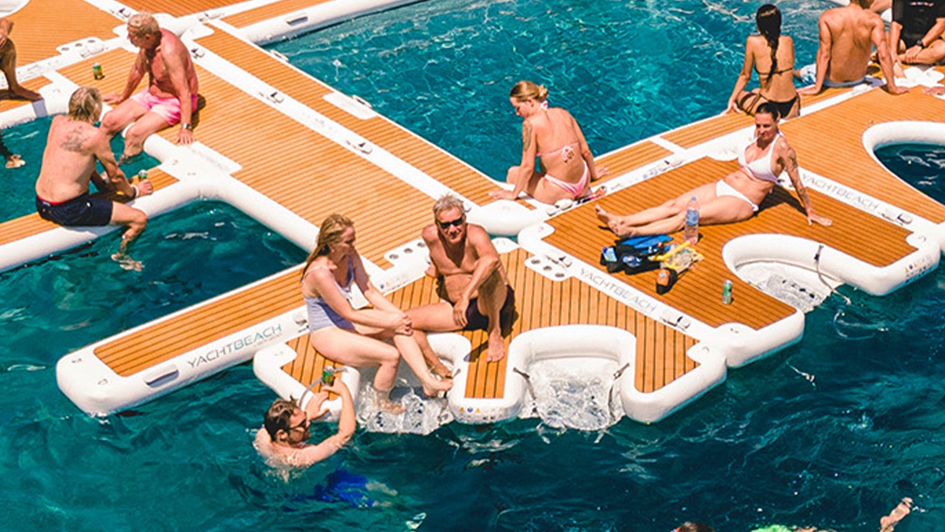 The photo shows how the Yacht Beach Multi Dock can be put on the other platforms. A lot of people are sitting on the platform, which is floating on the water.