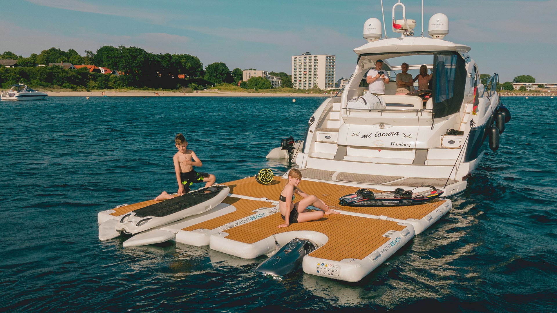 A boat on the water has several floating platforms attached to the back. A Seabob is parked on one of them.